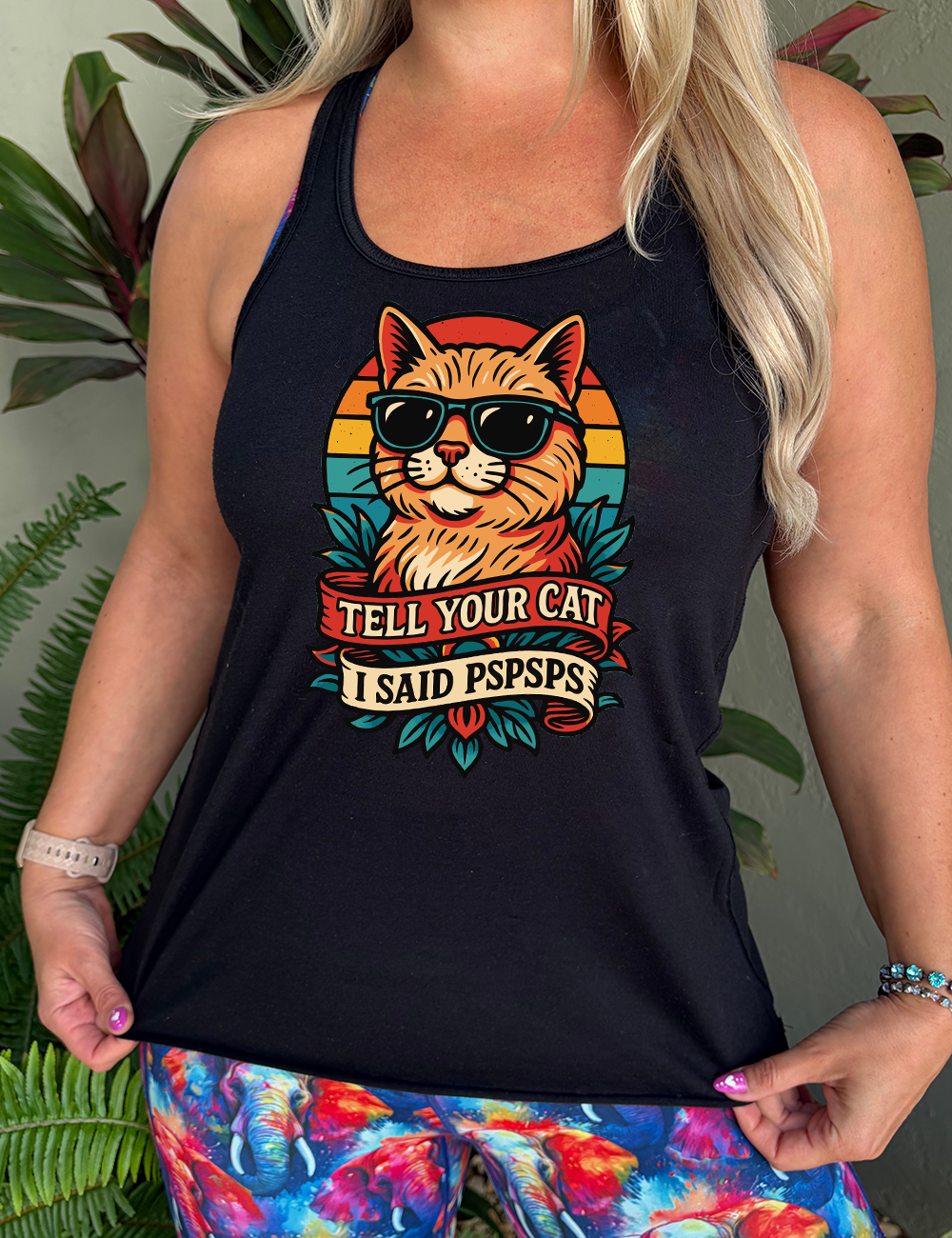 black racerback tank with the large graphic of a cat head and torso, wearing sunglasses, with a colorful background, and two banners below it with the words "tell your cat I said pspsps" on them