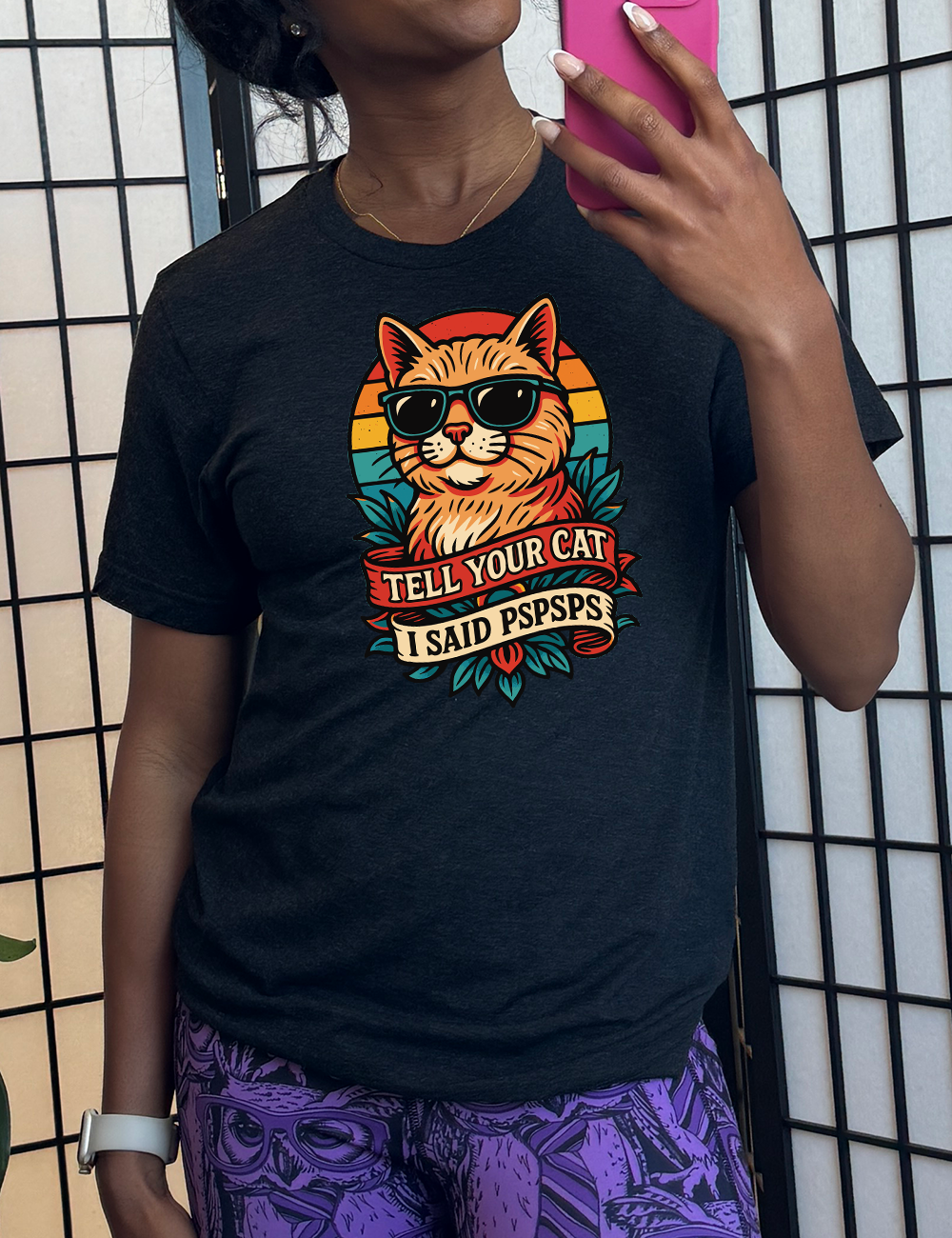 black unisex tee with the large graphic of a cat head and torso, wearing sunglasses, with a colorful background, and two banners below it with the words "tell your cat I said pspsps" on them