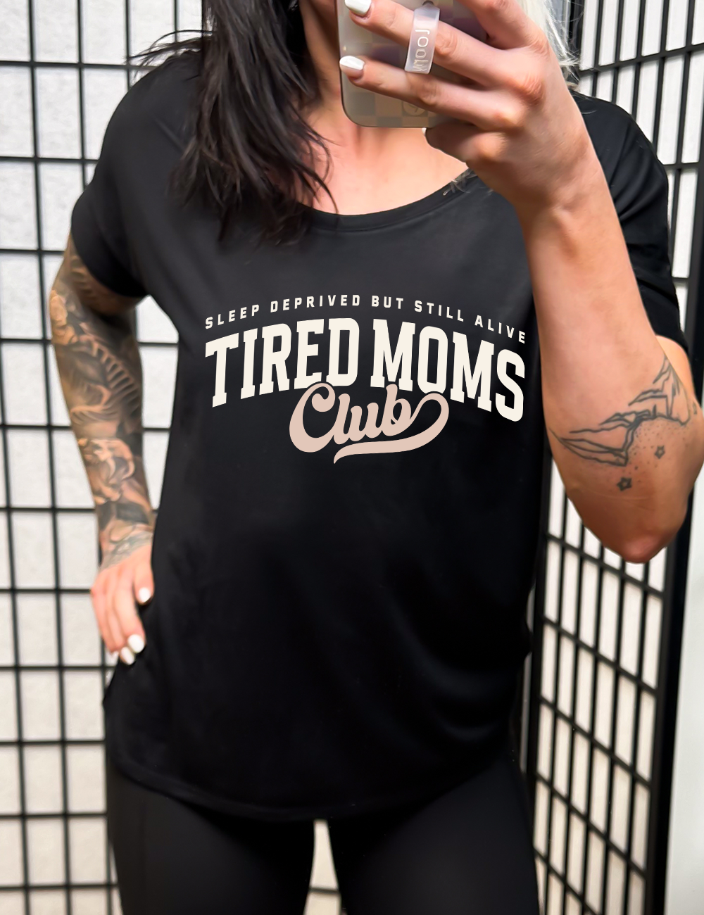 black slouchy tee with the words "sleep deprived but still alive" in smaller letters, and "tired moms club" in large letters