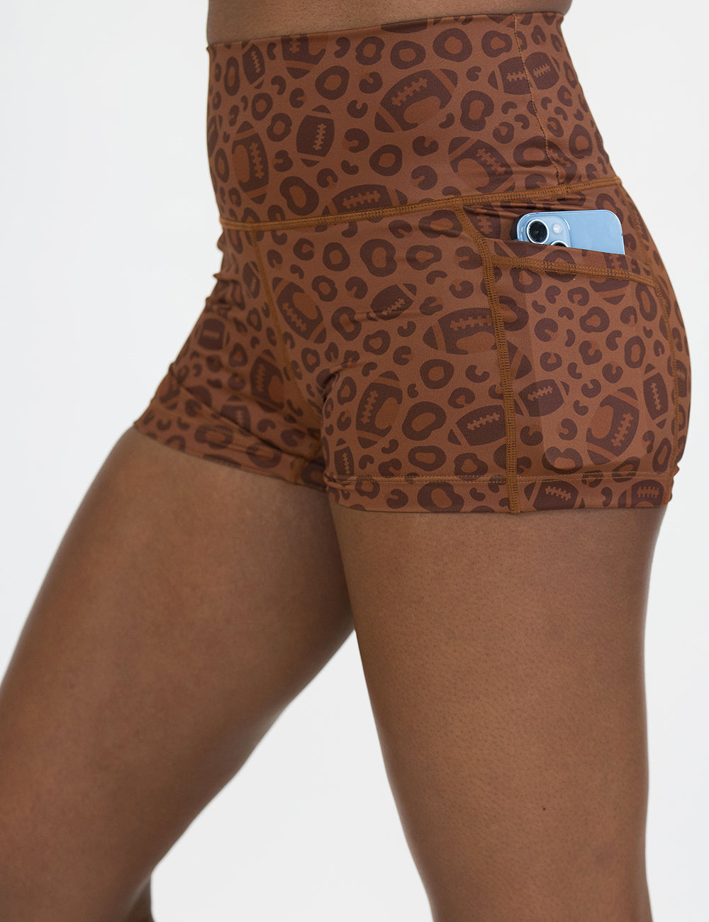 close up of the football themed brown leopard print 2.5 inch shorts with a phone in its pocket