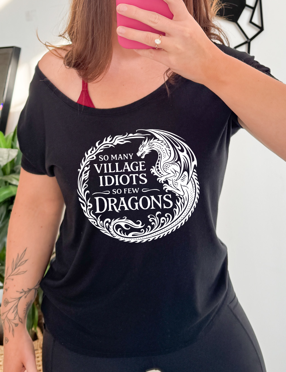 black slouchy tee with the graphic of a dragon, creating a circle from its tail plus flames, and the words "so many village idiots so few dragons" written within it