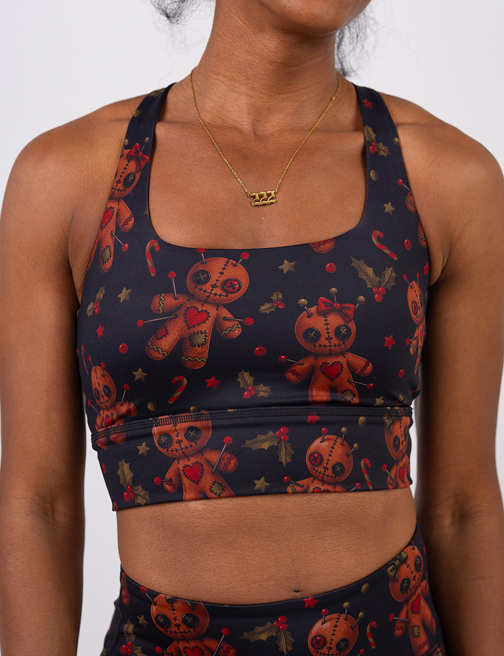 front of the gingerbread voodoo dolls with pins in them surrounded by berries and stars on a black background sports bra