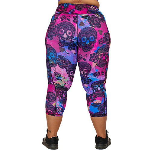 back view of capri length purple, pink and blue tie dye leggings with black skull and rose pattern