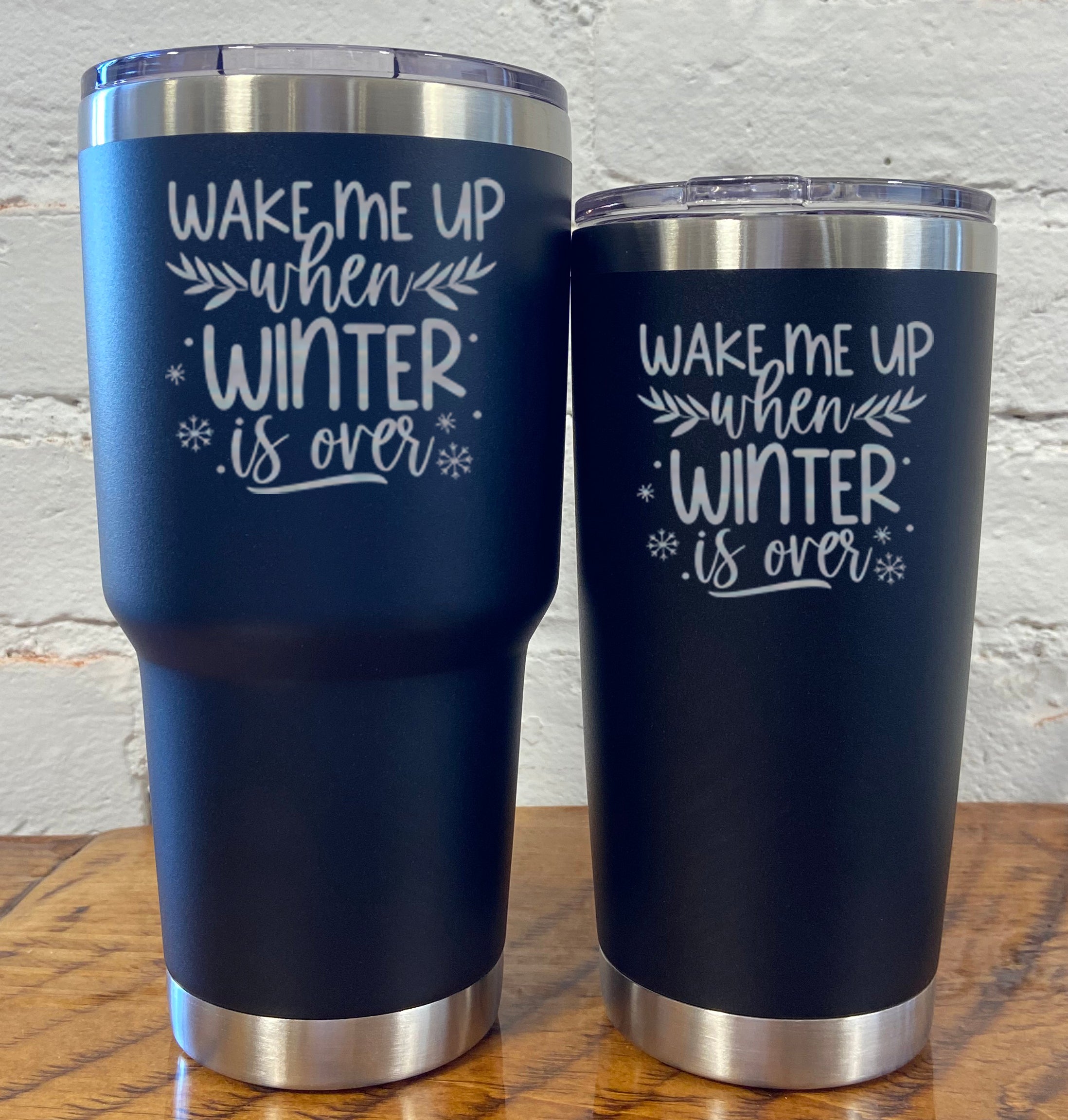 30oz and 20oz black tumblers with silver saying "wake me up when winter is over" with mini snowflakes around it