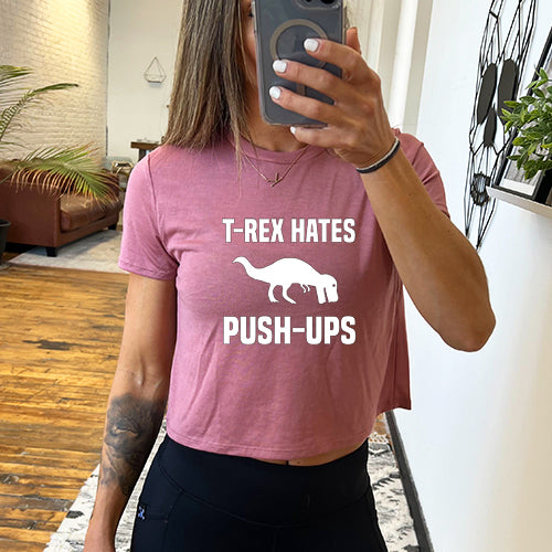 Model wearing a mauve colored cropped tee with a dinosaur and the saying "T-rex hates push-ups" on the front