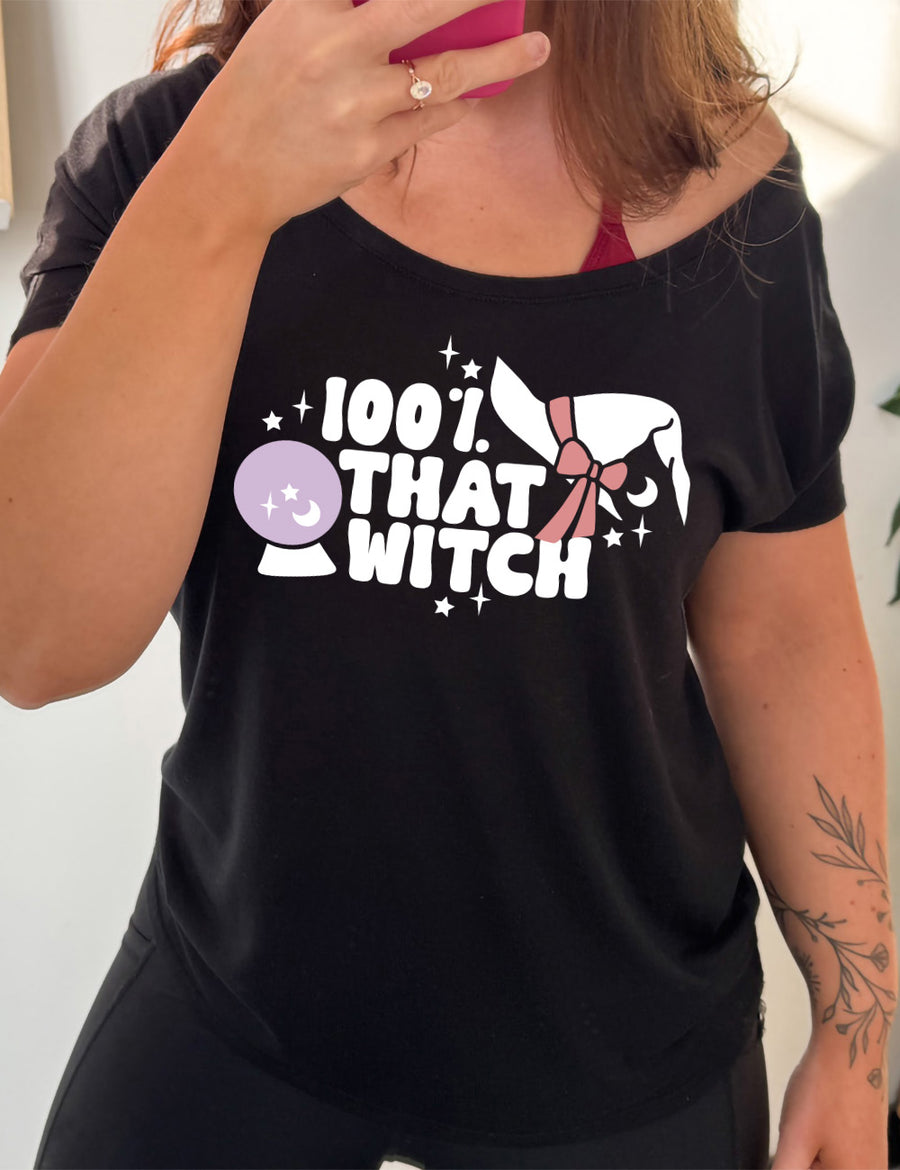 black slouchy tee with the words "100% that witch" next to the graphic of a witch hat with a bow, a crystal ball, and some stars