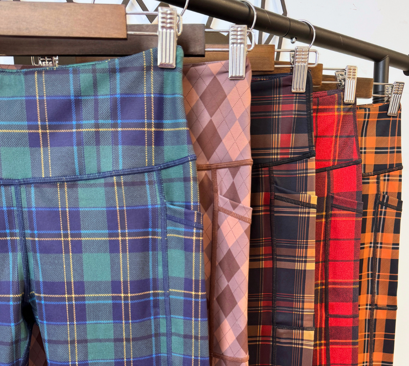 A close-up of multiple pairs of plaid leggings hanging from a black clothing rack with metal clips.