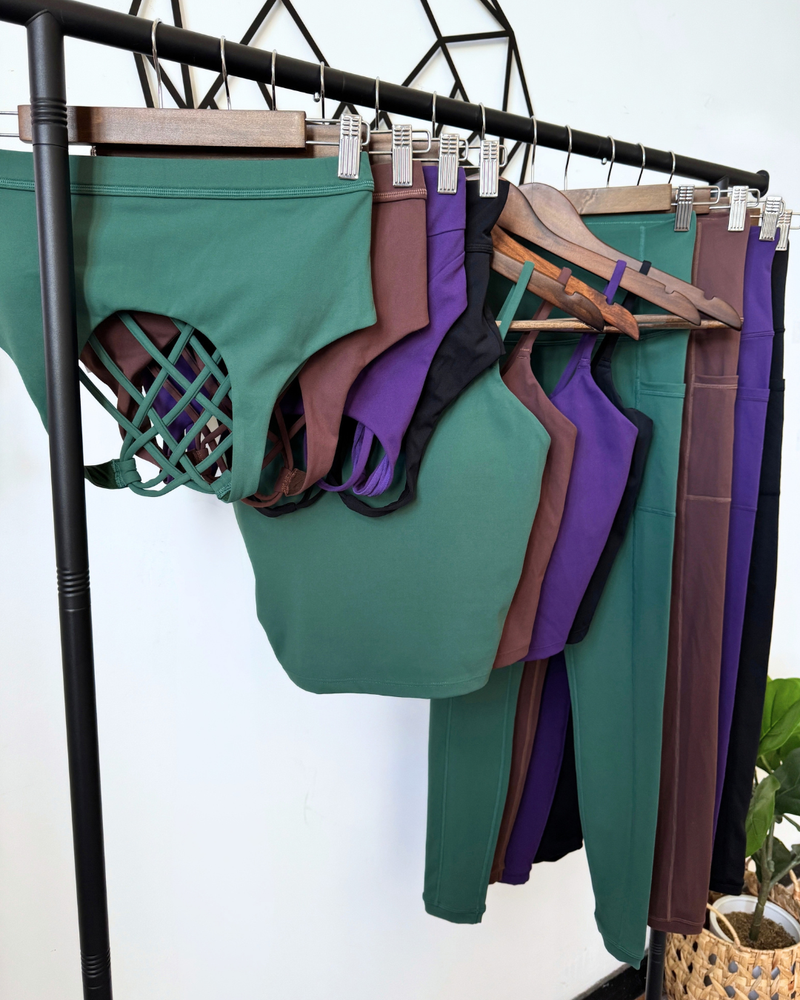 Athletic clothing in green, brown, purple, and black hanging on wooden hangers and clips from a black clothing rack