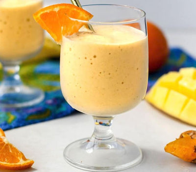 Glass of orange smoothie with a mango and orange wedge on a colorful tablecloth.