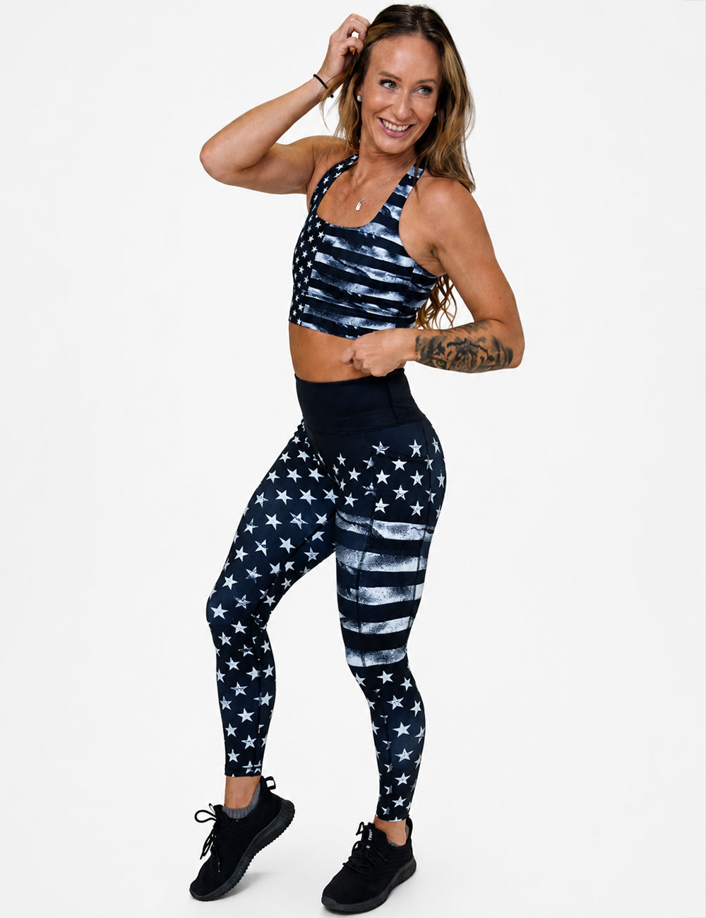 Model wearing the full length black leggings with a white stars and stripes pattern and the matching longline bra against a white background