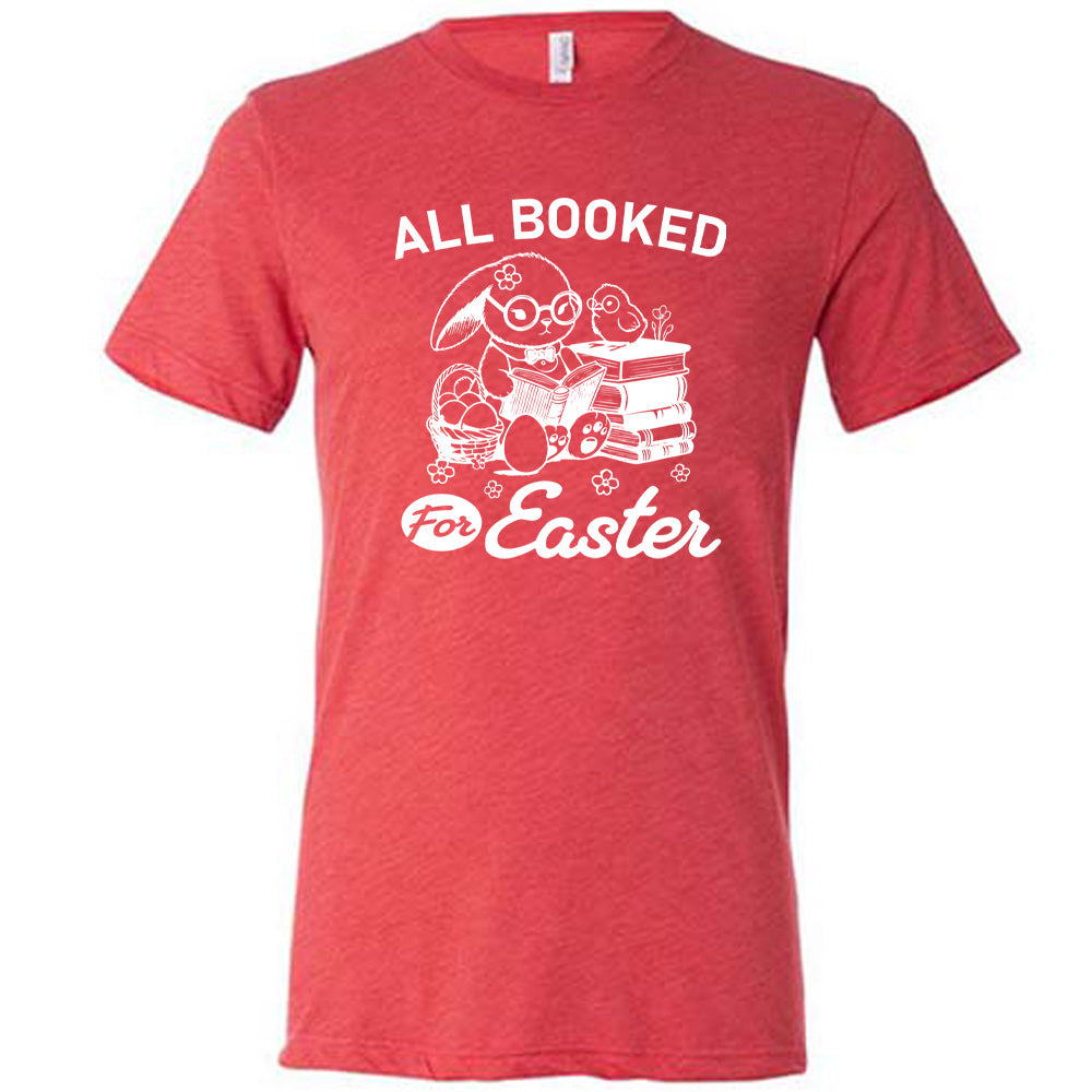 red unisex tee with the words "all booked for Easter" on it, and the graphic of a bunny wearing glasses and a bowtie, reading a book, next to a stack of books (with a bird wearing glasses on top of it) on one side, and a basket of eggs on the other side
