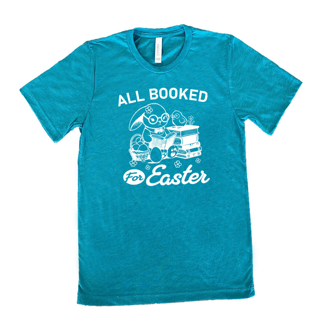 teal unisex tee with the words "all booked for Easter" on it, and the graphic of a bunny wearing glasses and a bowtie, reading a book, next to a stack of books (with a bird wearing glasses on top of it) on one side, and a basket of eggs on the other side