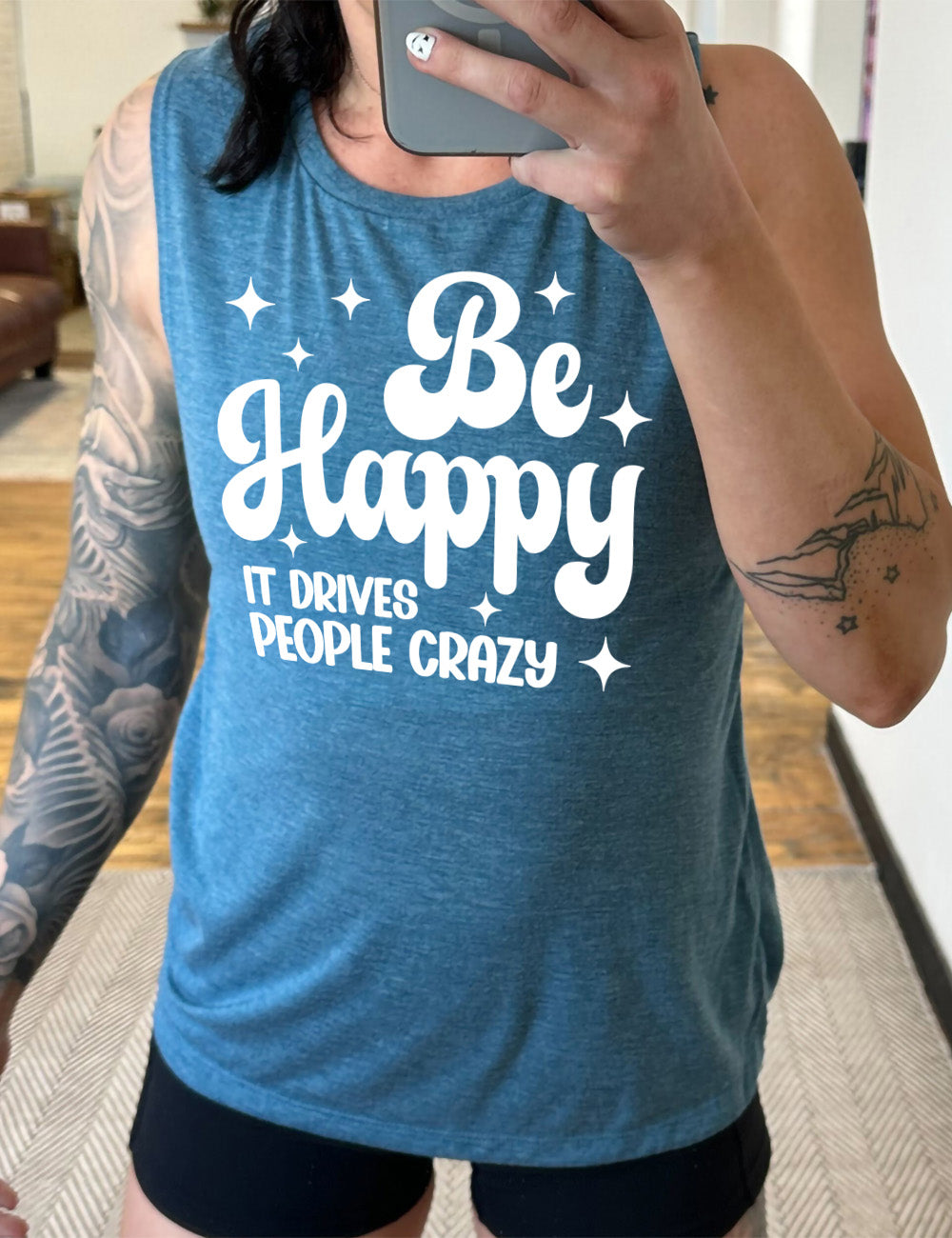 deep teal muscle tank with the words "be happy it drives people crazy" on it, with a number of stars around