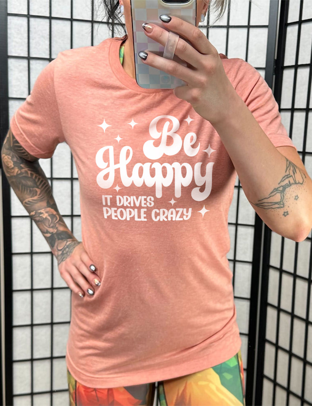 sunset unisex tee with the words "be happy it drives people crazy" on it, with a number of stars around