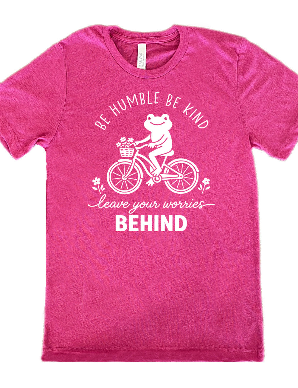 berry unisex tee with the graphic of a happy frog riding a bike that has a basket of flowers attached, with a flower in front and behind the bike, and the wording arching above and ending below saying "be humble be kind leave your worries BEHIND"