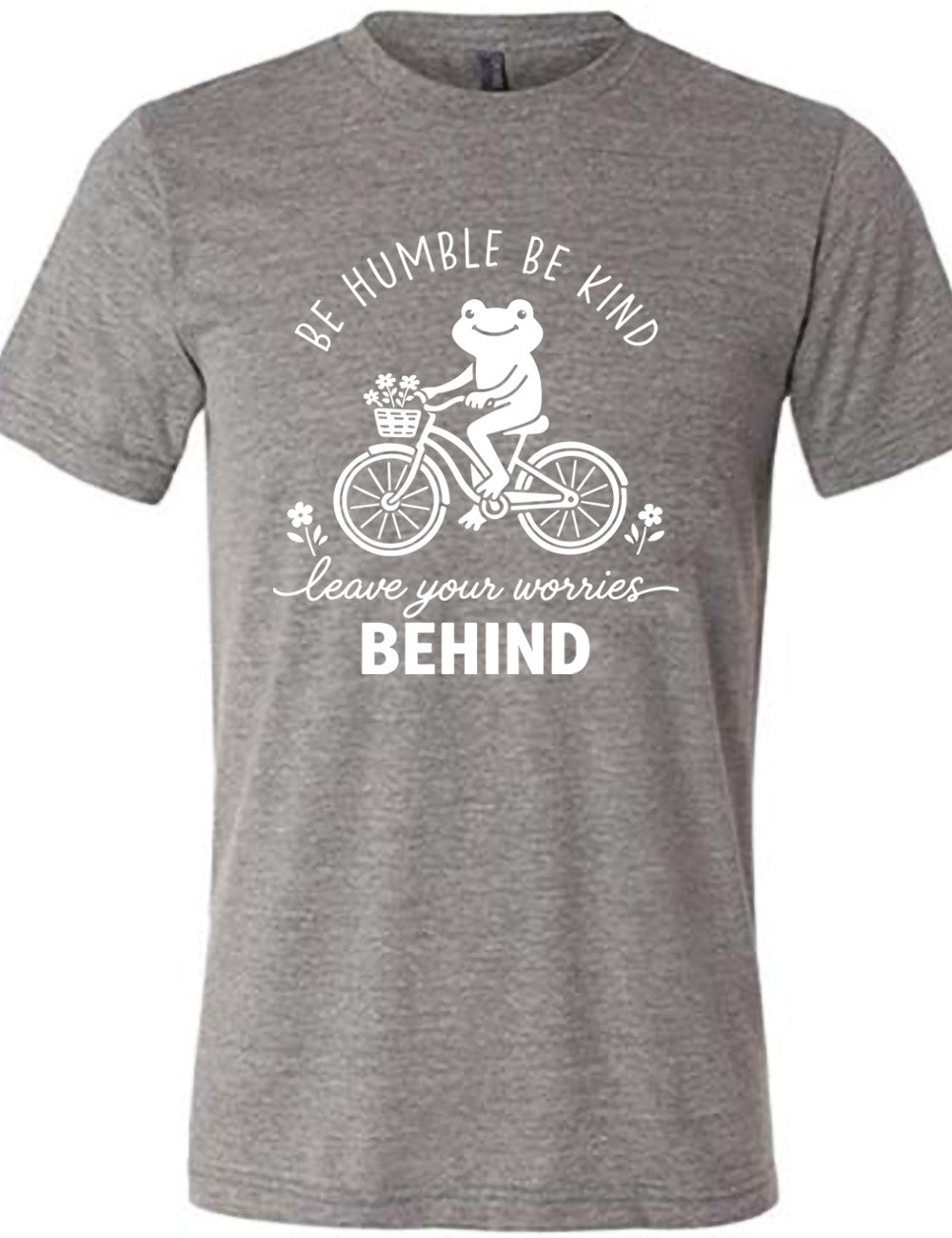 grey unisex tee with the graphic of a happy frog riding a bike that has a basket of flowers attached, with a flower in front and behind the bike, and the wording arching above and ending below saying "be humble be kind leave your worries BEHIND"