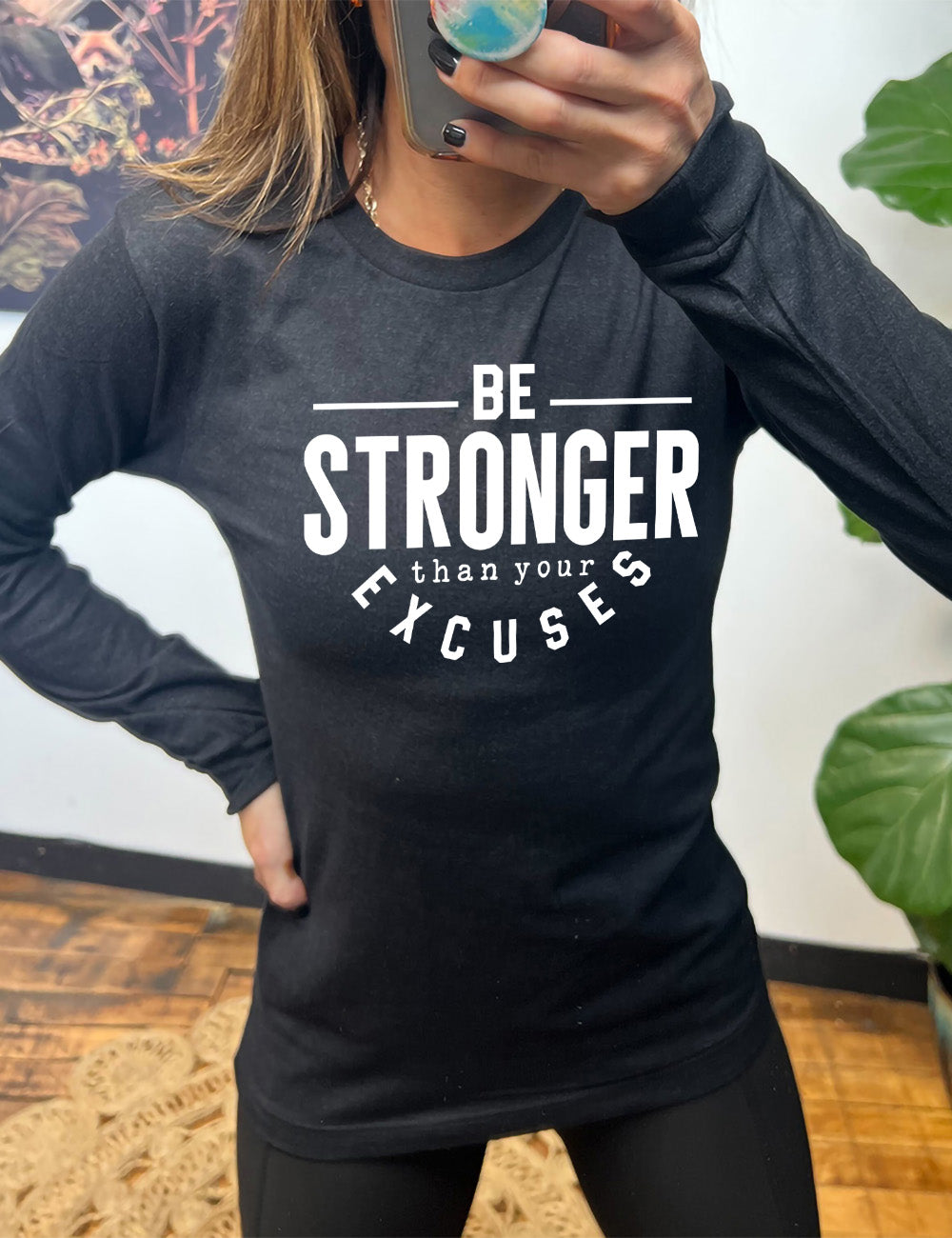 heather black long sleeve tee with words on it saying "be STRONGER than your excuses", with lines in front and after the word "be", the word "stronger" in the largest font, and the word "excuses" arching 