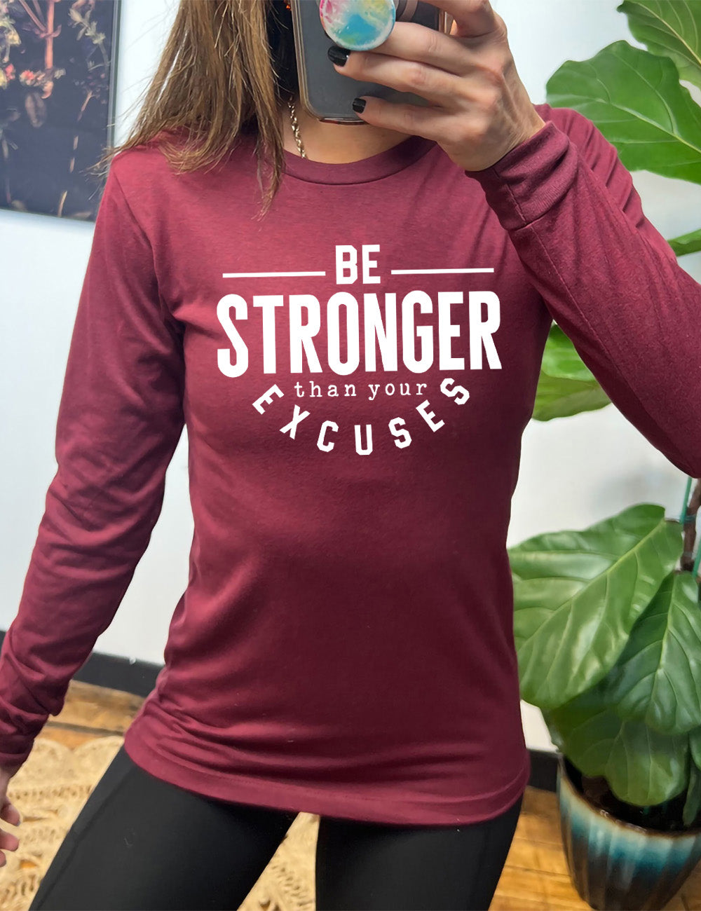 heather cardinal long sleeve tee with words on it saying "be STRONGER than your excuses", with lines in front and after the word "be", the word "stronger" in the largest font, and the word "excuses" arching 