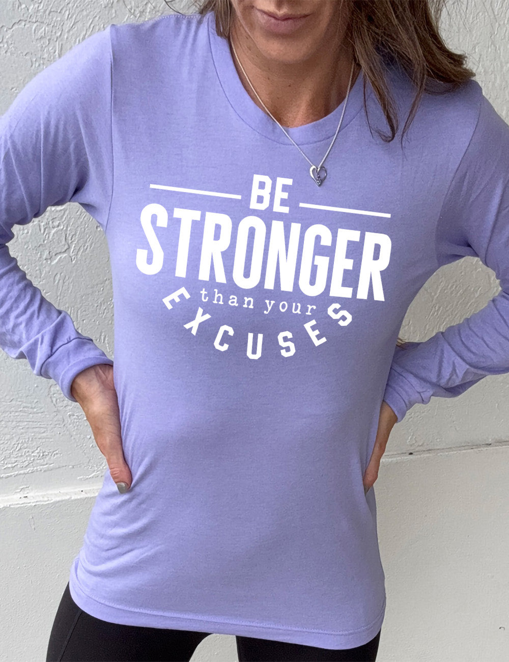 heather dark lavender long sleeve tee with words on it saying "be STRONGER than your excuses", with lines in front and after the word "be", the word "stronger" in the largest font, and the word "excuses" arching 