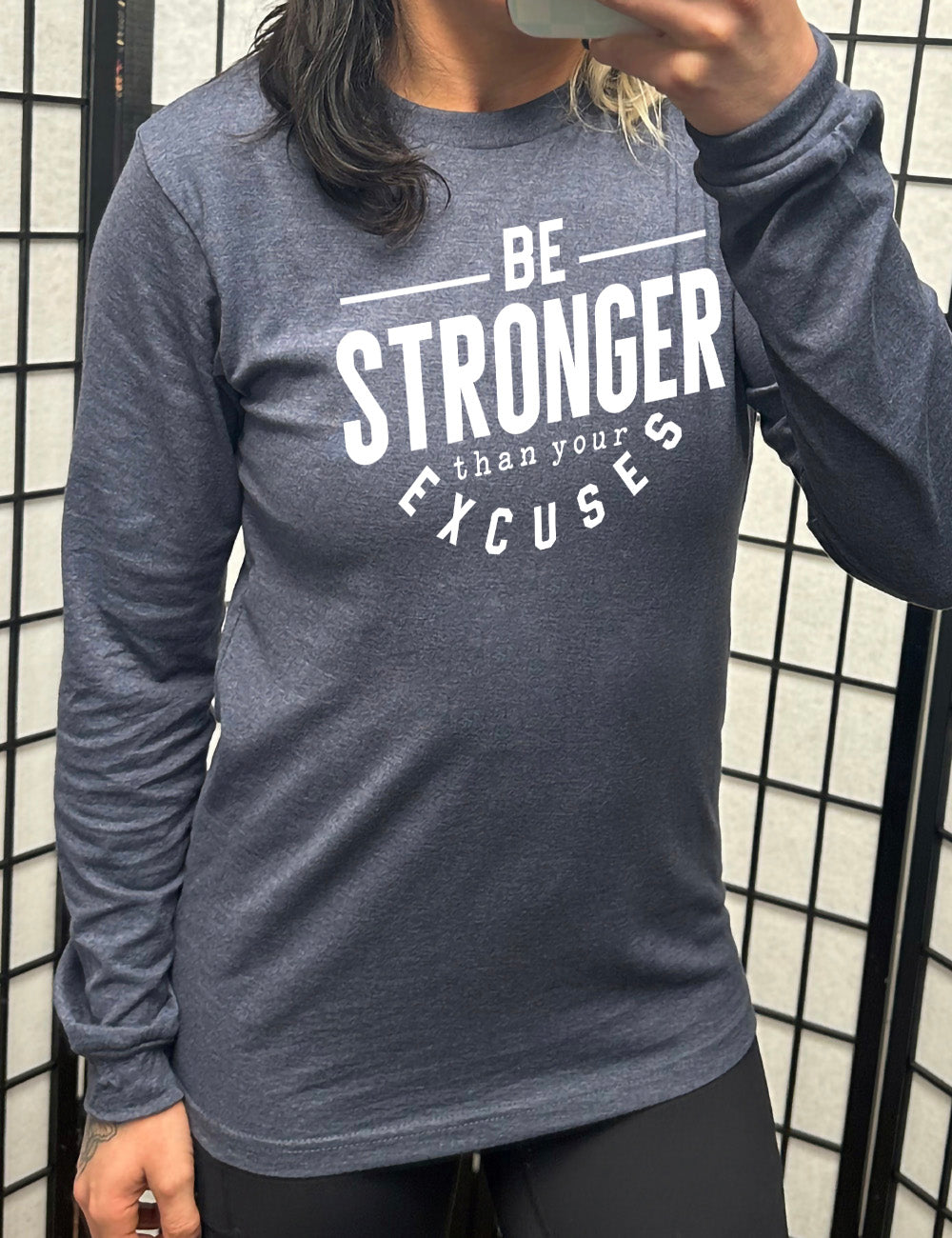 heather navy long sleeve tee with words on it saying "be STRONGER than your excuses", with lines in front and after the word "be", the word "stronger" in the largest font, and the word "excuses" arching 