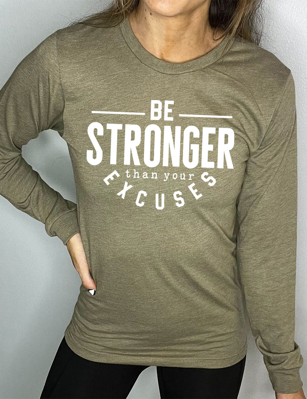 heather olive long sleeve tee with words on it saying "be STRONGER than your excuses", with lines in front and after the word "be", the word "stronger" in the largest font, and the word "excuses" arching 