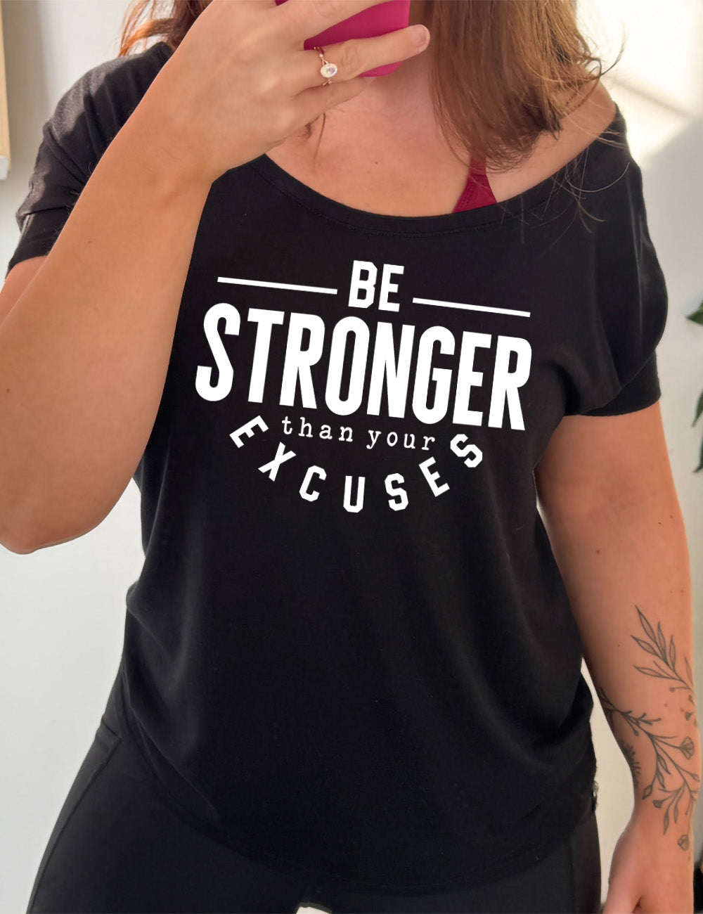 black slouchy tee with words on it saying "be STRONGER than your excuses", with lines in front and after the word "be", the word "stronger" in the largest font, and the word "excuses" arching 