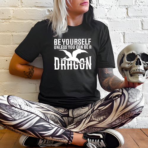 model wearing a black unisex shirt with the saying "Be Yourself Unless You Can Be A Dragon" on it in white