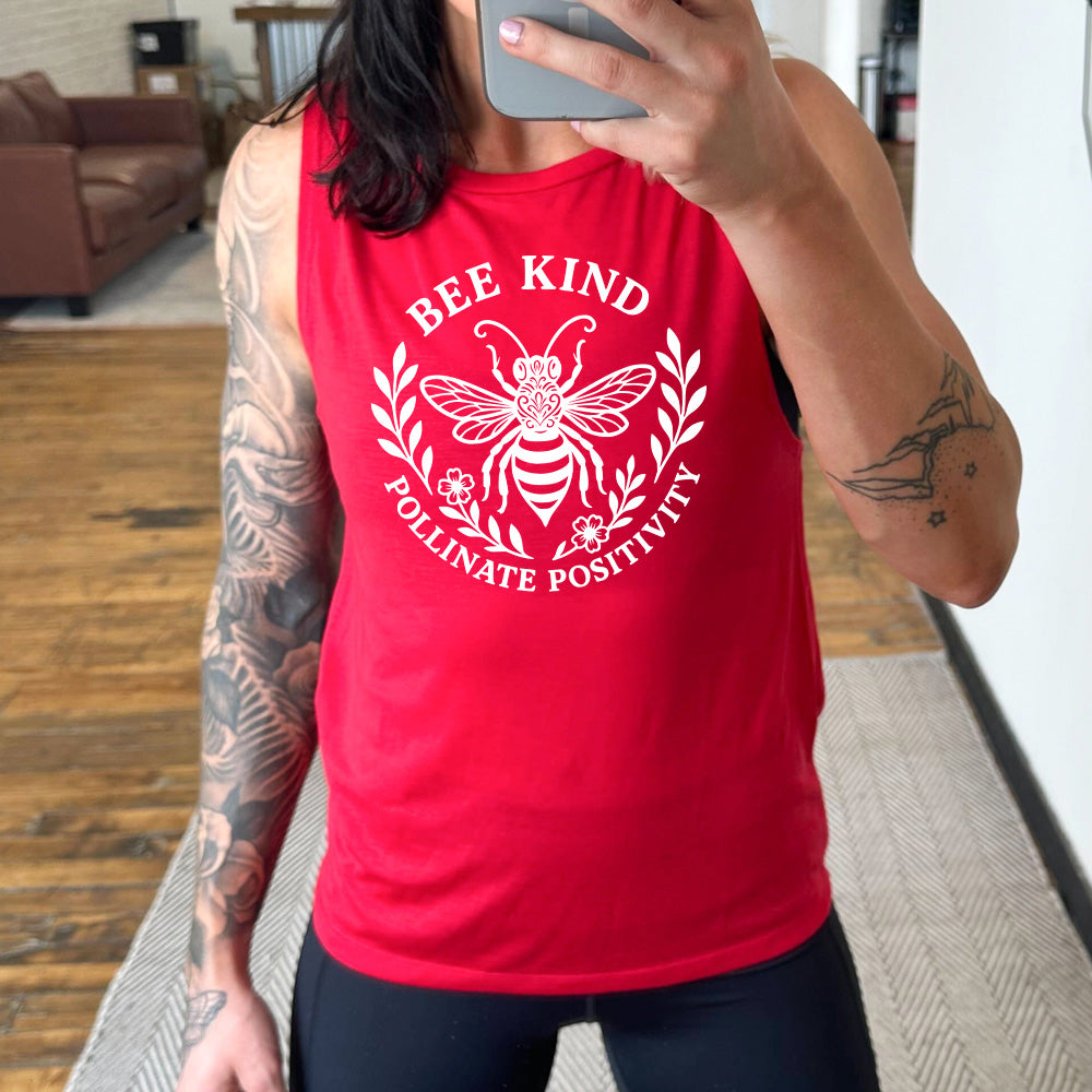 red muscle tank with the words "bee kind pollinate positivity" on it, arranged in two arcs, forming a circled effect, with two branches and two flowered branches within the circle, and a large fancy bee in the center
