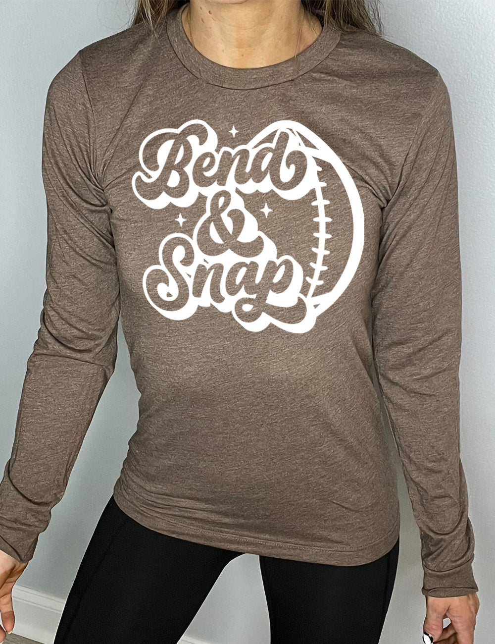heather brown long sleeve tee with the words in cursive saying "Bend & Snap" with the outline graphic of a football slightly underneath