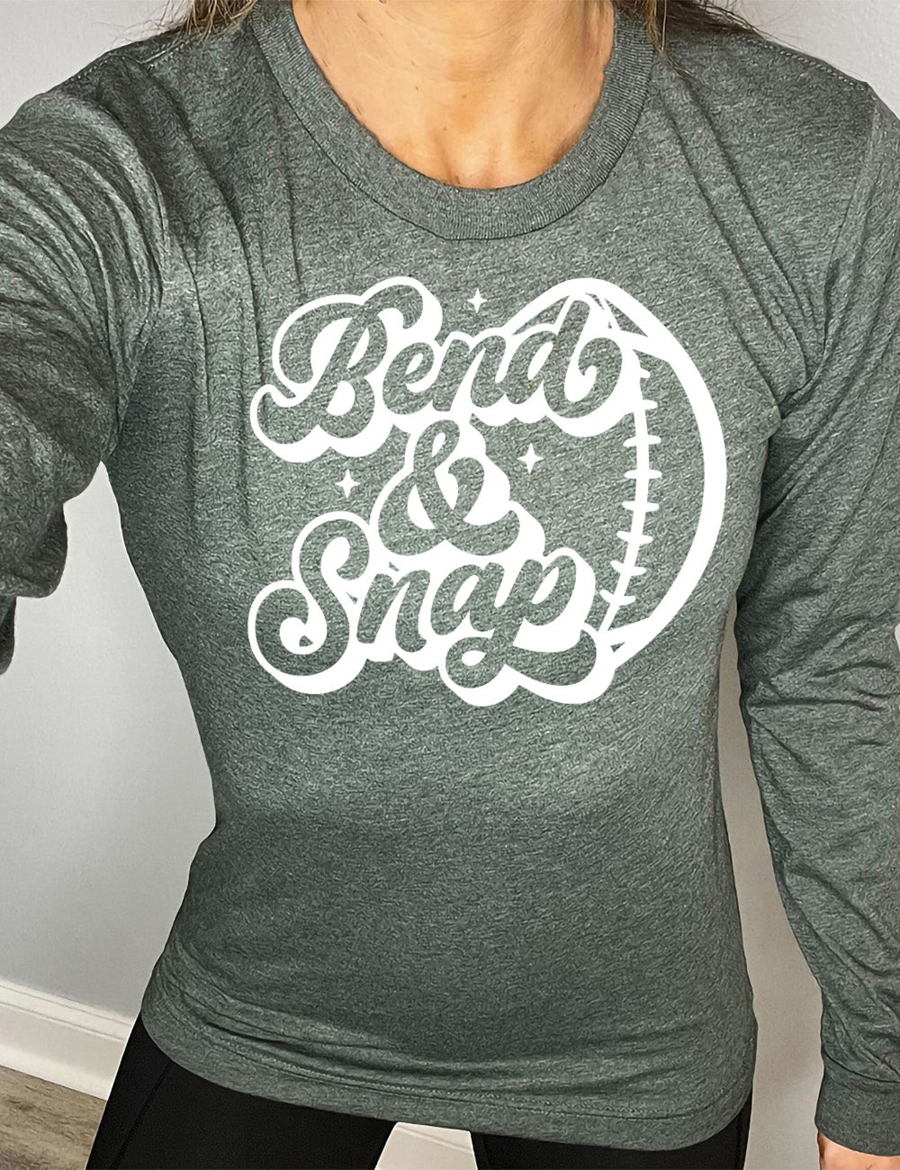 heather forest long sleeve tee with the words in cursive saying "Bend & Snap" with the outline graphic of a football slightly underneath