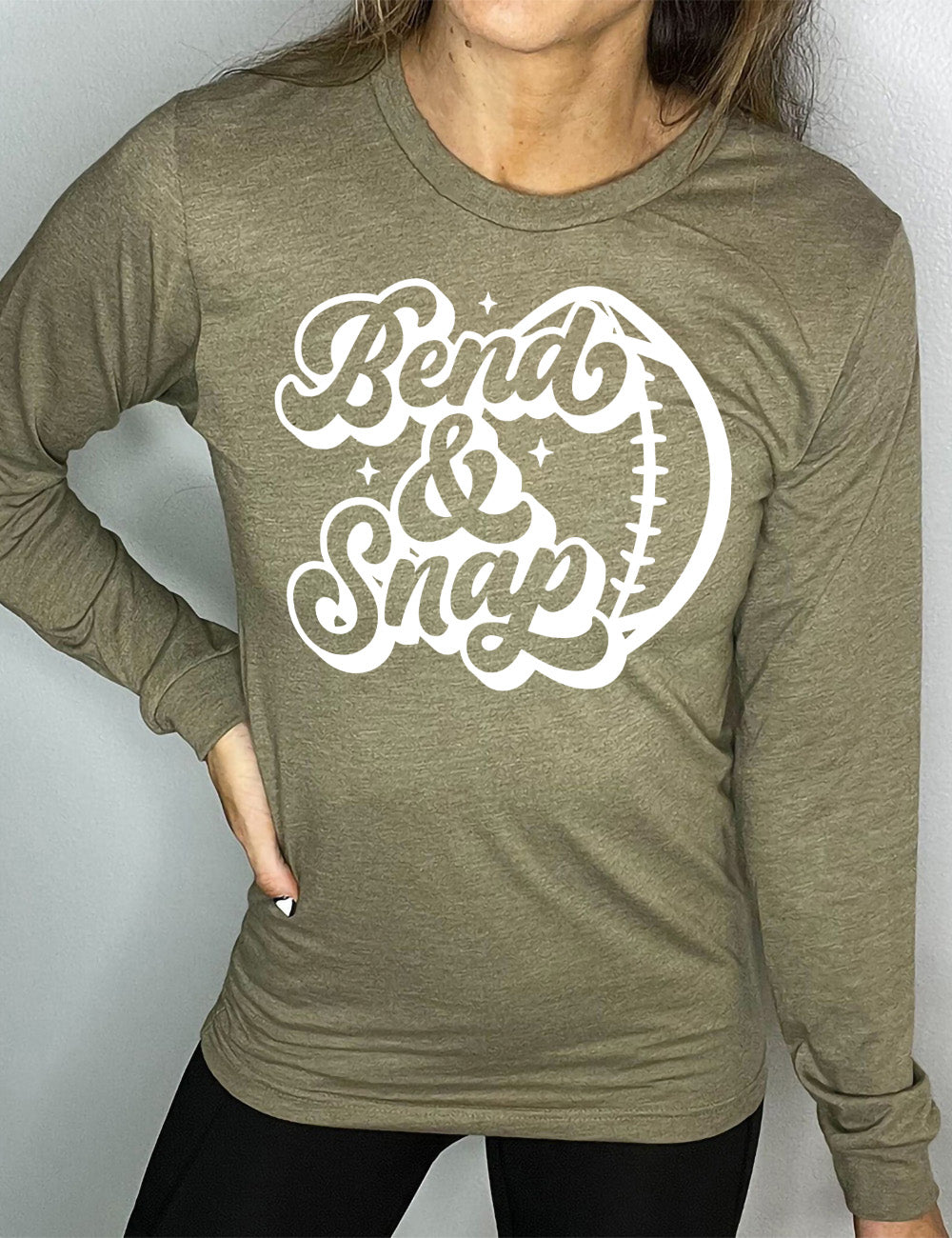 heather olive long sleeve tee with the words in cursive saying "Bend & Snap" with the outline graphic of a football slightly underneath