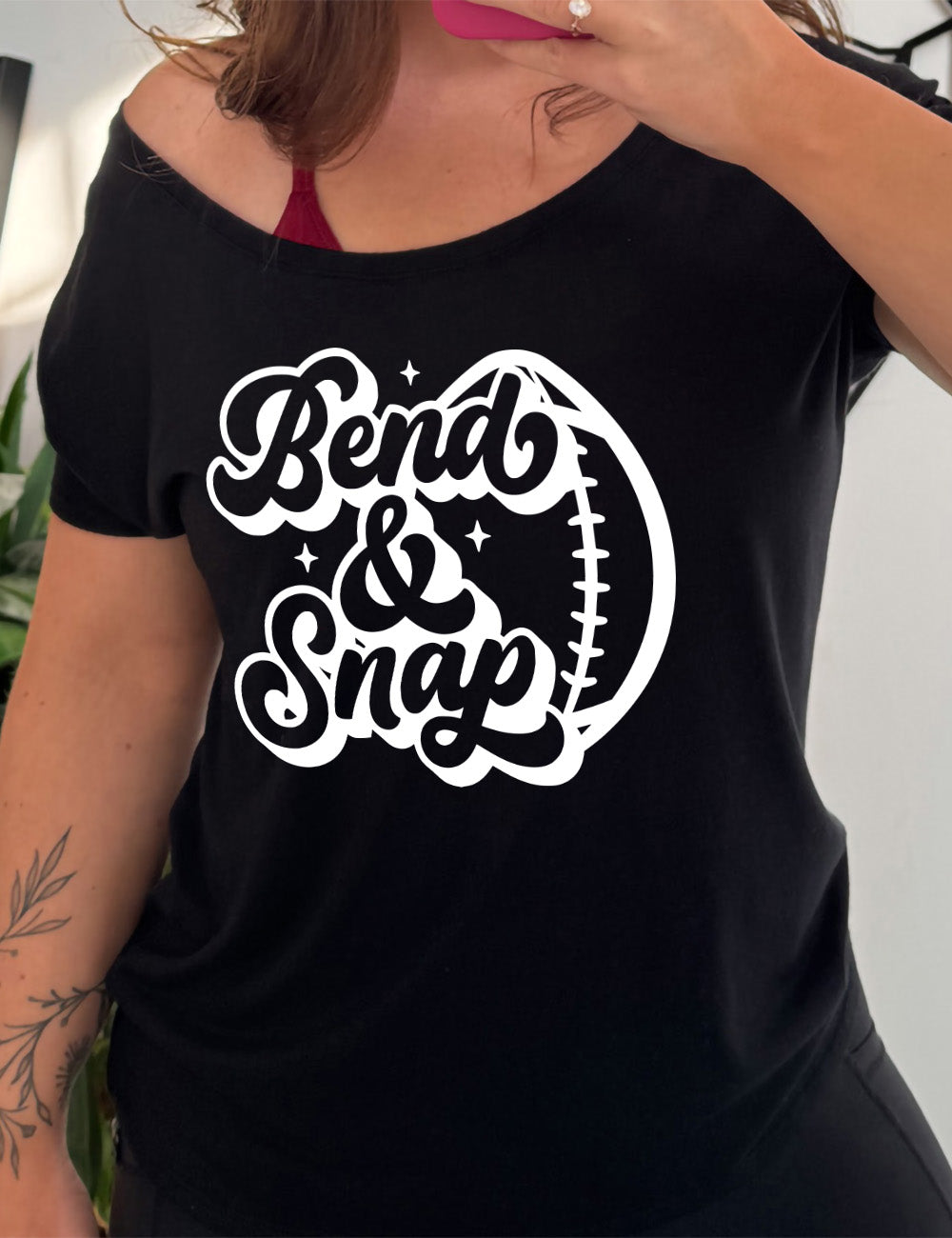 black slouchy tee with the words in cursive saying "Bend & Snap" with the outline graphic of a football slightly underneath