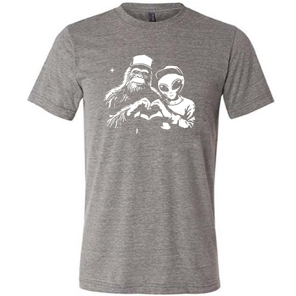 Grey colored shirt with bigfoot and alien doing heart hands graphic on it