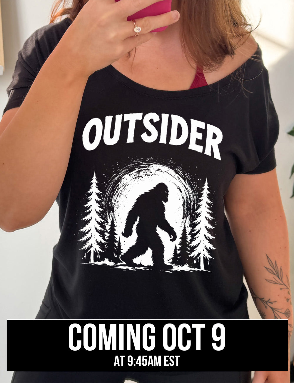 black slouchy tee with the graphic of bigfoot, silhouetted against a large moon, walking through pine trees, and a word above it saying "OUTSIDER" Coming October 9th