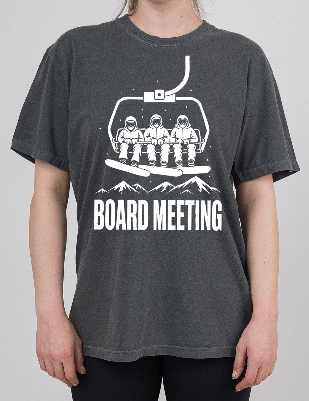 pepper modern tee with the graphic of three snowboarders riding a ski lift, with snowy mountains in the distance and little dots of snow around, and words underneath this saying "board meeting" in capital letters