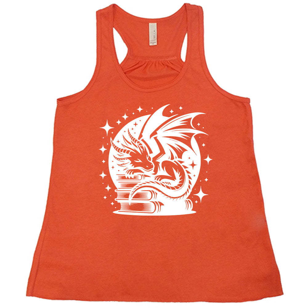 coral racerback tank with the graphic of a dragon resting on a stack of books, in front of a full moon, with many stars around