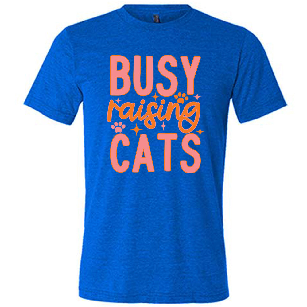 blue unisex tee with the words "busy raising cats" on it, with graphics of a couple small paw prints and a number of little stars