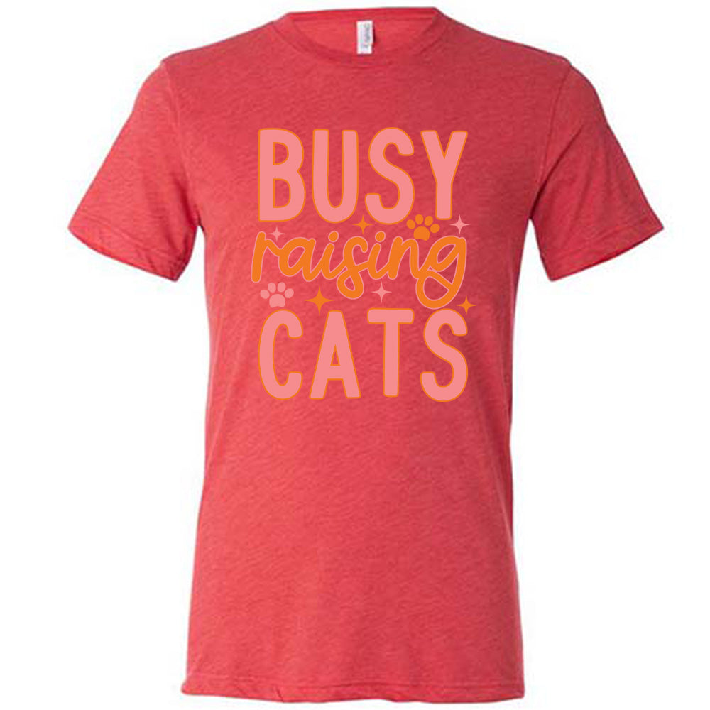 red unisex tee with the words "busy raising cats" on it, with graphics of a couple small paw prints and a number of little stars