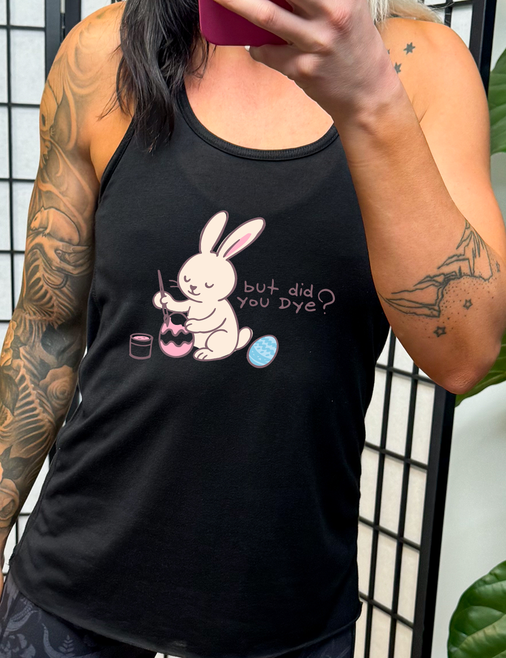 black racerback tank with the graphic of a bunny happily creating an Easter egg, with the words "but did you dye?" on it