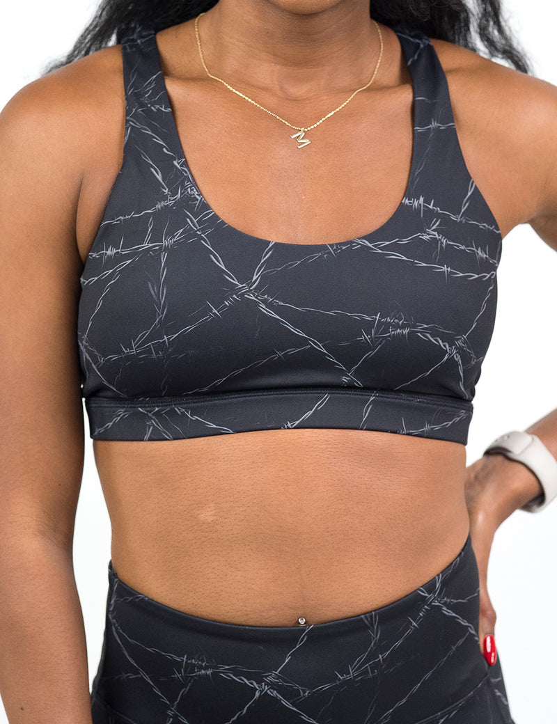 Person wearing a black sports bra with  a white barbed wire pattern on it