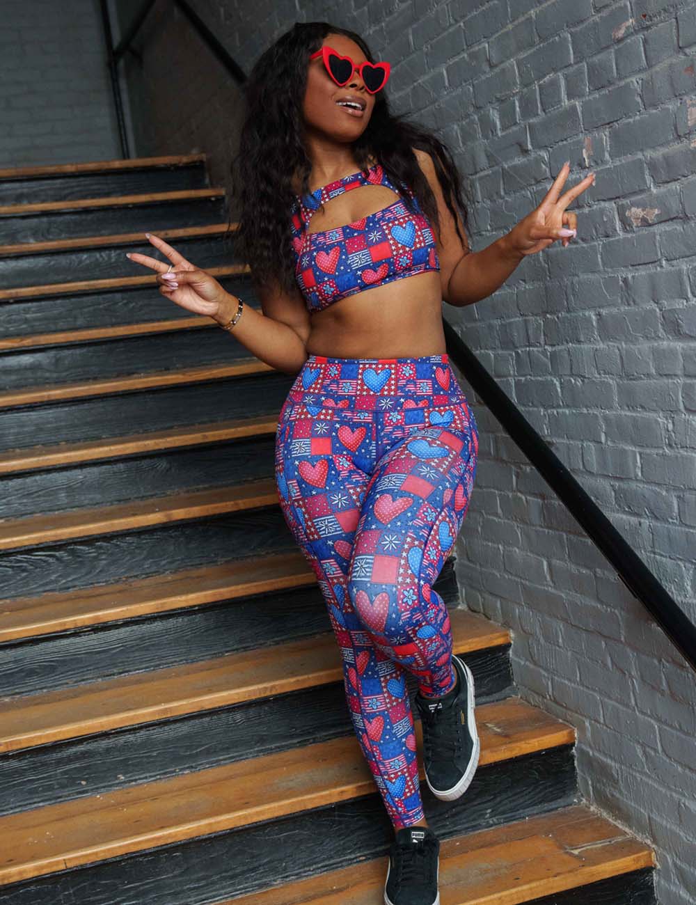 model wearing the red white and blue with hearts and flowers patchwork pattern leggings and bra posing in a staircase