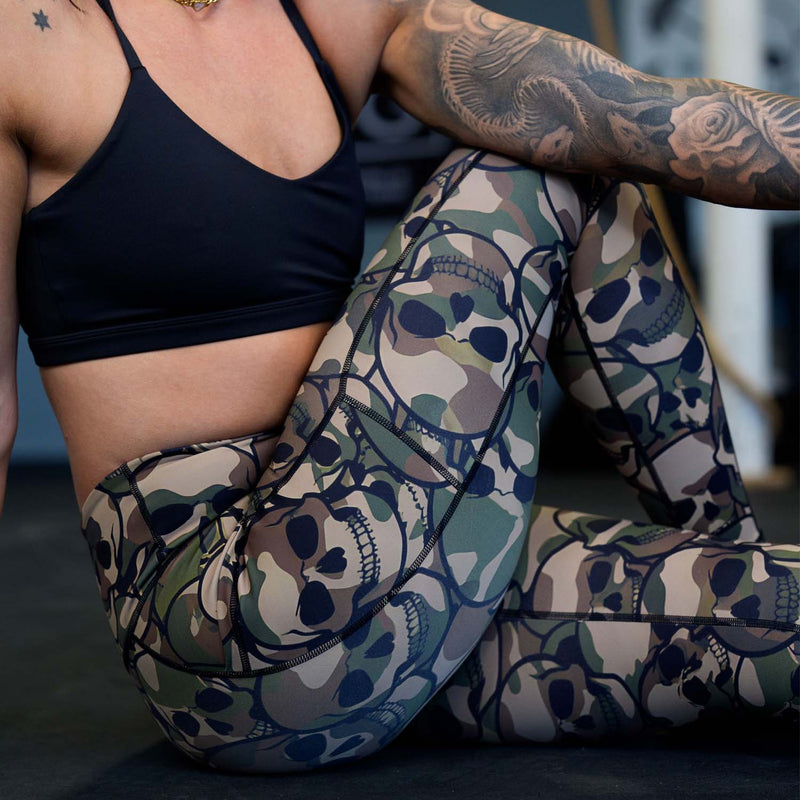 Person wearing a black sports bra and camouflage-patterned pants with skull designs.