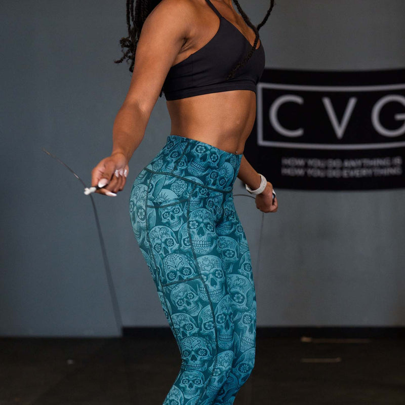 Person wearing teal patterned skull pants and black sports bra holding a jump rope.