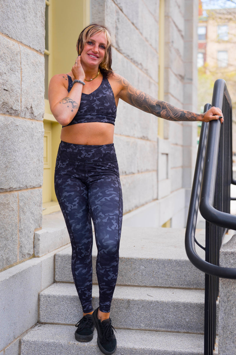 A woman wearing a matching camouflage athletic set stands on outdoor stone steps