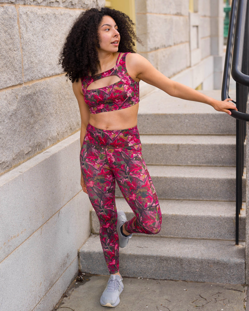 A woman with curly black hair stands on outdoor stone stairs wearing a matching camo print activewear set consisting of a sports bra and high-waisted leggings.