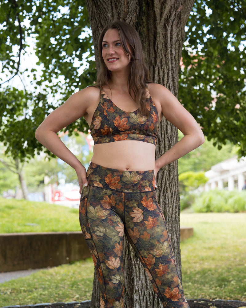 A woman posing outdoors in a matching floral print activewear set consisting of a sports bra and high-waisted leggings, standing next to a tree in a park.