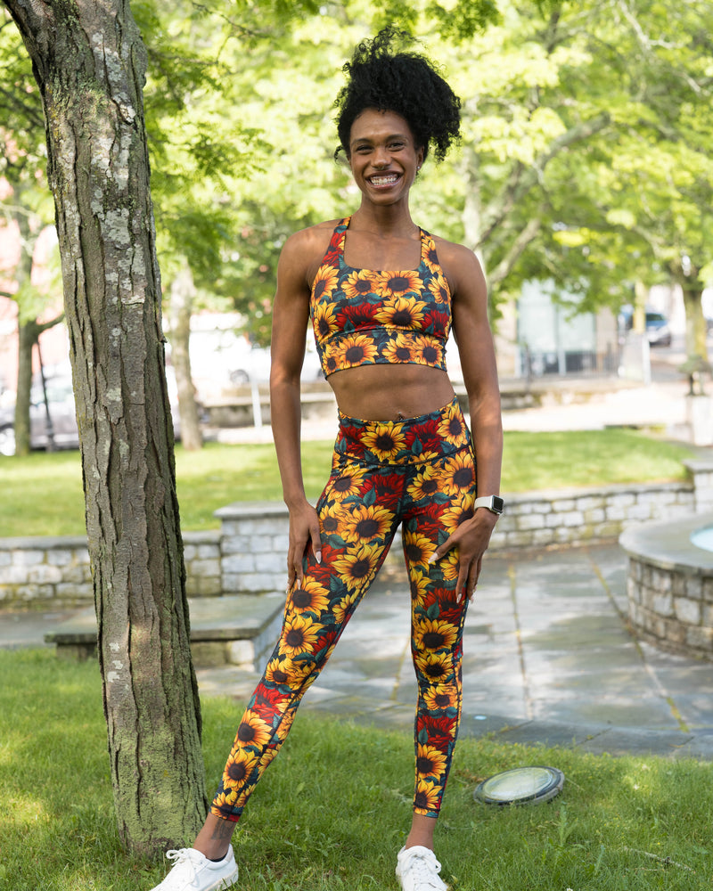 A woman stands outdoors in a park wearing a matching sunflower-print activewear set