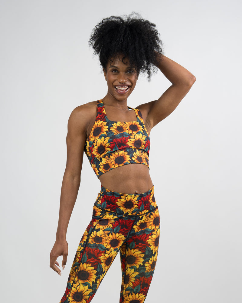 A woman modeling a matching sunflower print activewear set against a plain white studio background.