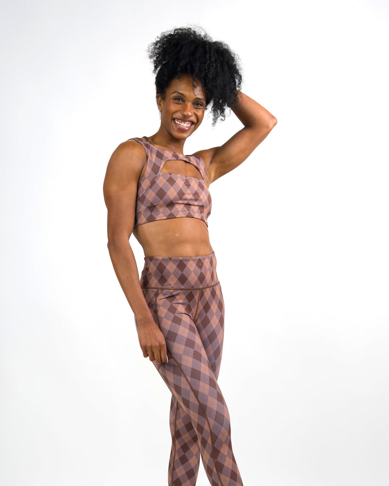 A woman modeling a matching two-piece athletic set with a dusty rose and purple plaid pattern against a plain white studio background.