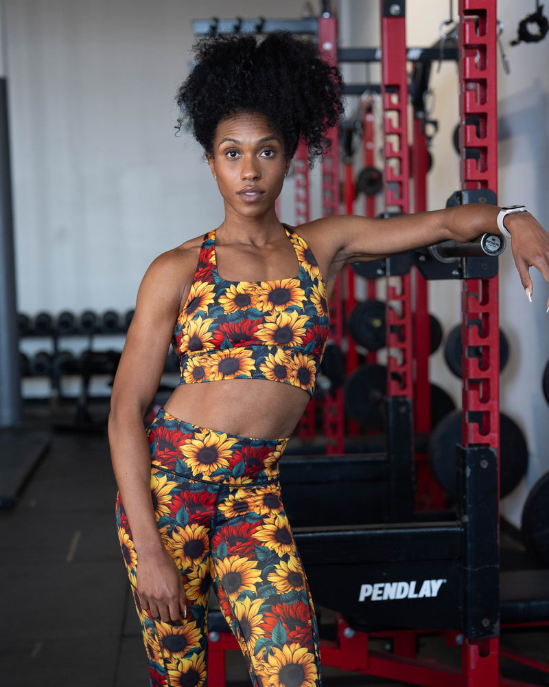 A woman posing in a gym wearing a matching two-piece activewear set with a vibrant sunflower print.